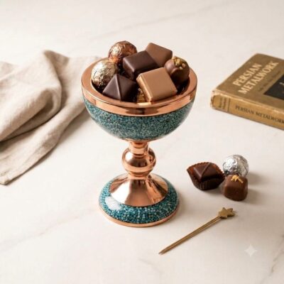 Handmade Persian turquoise inlay copper goblet filled with assorted gourmet chocolates on a white marble surface.