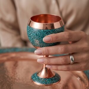 Detailed hand holding a turquoise inlayed copper drinking cup with smooth finish