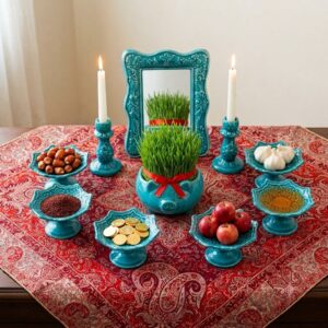 Turquoise Hamedan enamel Haft-sin set arranged on red Persian tapestry cloth with candles lit.