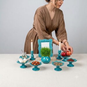 Close-up of a woman adding fresh red apples to a blue Lalejin enamel pedestal dish.