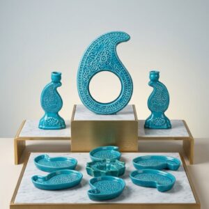 Studio display of the turquoise Hamedan enamel pottery Haft-sin set on marble risers.