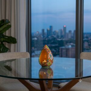 Enamel pottery candlestick holder reflecting light against a glass table and city view.