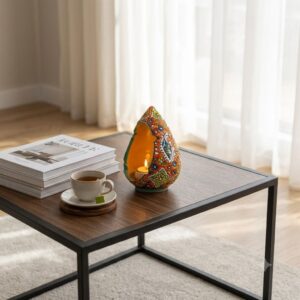 Handcrafted teardrop enamel candle holder on a modern coffee table near sunlit curtains.