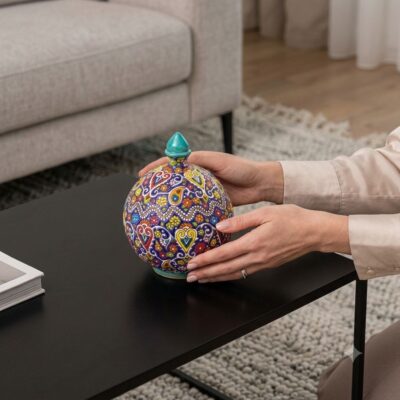 Woman placing a vibrant hand-painted Persian candy dish on dark table.