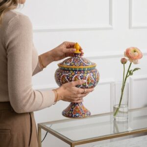 Woman holding Lalejin enamel pottery vessel beside vase of flowers