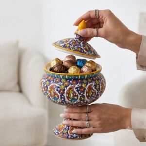 Close-up of hands opening decorative enamel pottery candy jar with chocolates