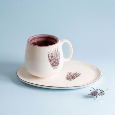 Handmade lavender coffee mug filled with hot dark coffee on a light blue background.