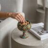 Hand-painted Hamedan enamel pottery nut bowl on concrete table with hand reaching for pistachios.