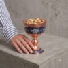 Hand holding a Persian handcrafted Copper and Pardaz nut bowl filled with pistachios on a concrete surface.