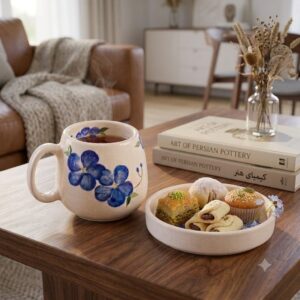 Steaming blue floral ceramic mug with a saucer filled with baklava and pastries next to art books.
