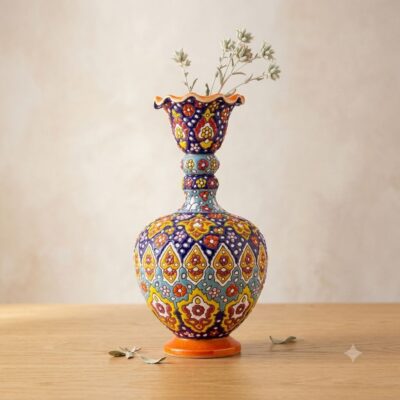 Full view of a decorated Hamedan enamel ceramic vase with simple dried stems on a light wood surface.