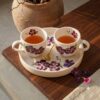 Hand-painted violet ceramic coffee cups with matching serving tray and golden spoon on a wooden table.