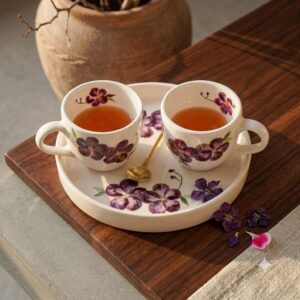Hand-painted violet ceramic coffee cups with matching serving tray and golden spoon on a wooden table.
