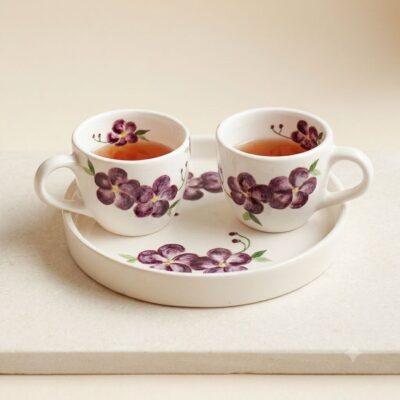 Pair of handcrafted cream ceramic cups with purple violet painting on a stone slab.