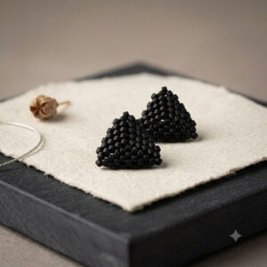 Pair of 3D woven matte black triangle beaded stud earrings displayed on textured artisan paper.