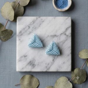 Pair of light blue 3D triangle beaded earrings placed on a white marble slab.