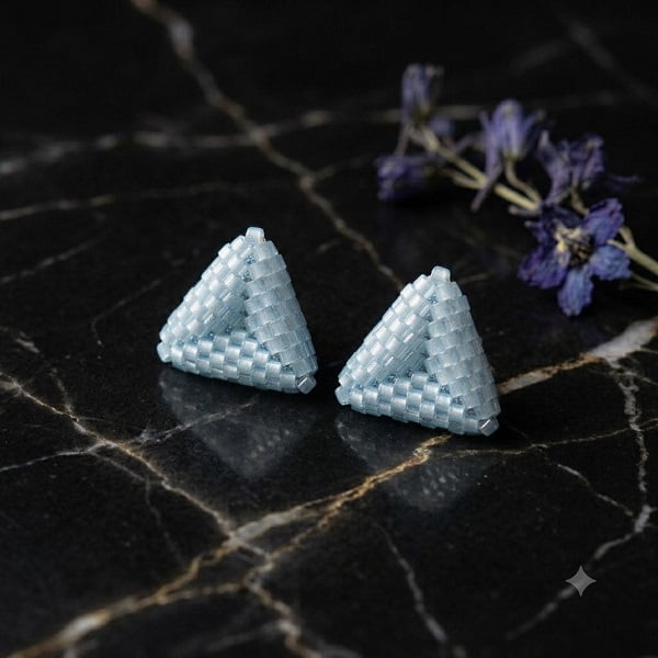 Close-up photo of sky-blue 3D triangle beaded stud earrings on dark marble background.