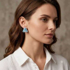 Brunette woman wearing gold-toned accent blue 3D beaded triangle earrings with a white linen shirt.