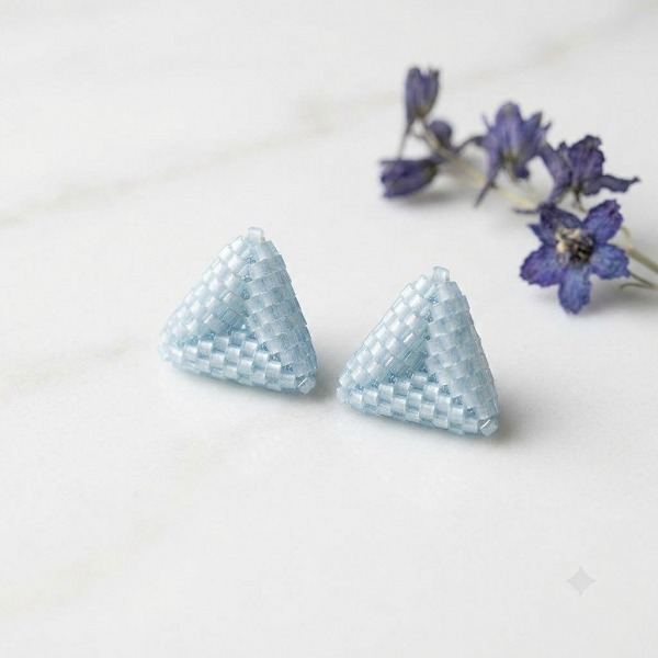 Sky-blue 3D beaded triangle stud earrings resting on a light marble surface.