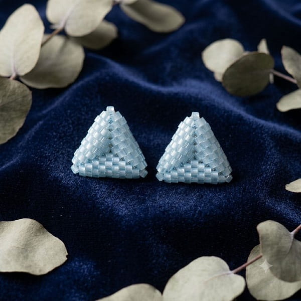 Light blue 3D beaded triangle stud earrings displayed on navy blue velvet fabric.