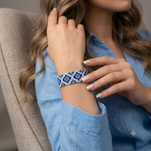 Woman wearing a handmade blue and gold-toned mosaic pattern beaded cuff bracelet.