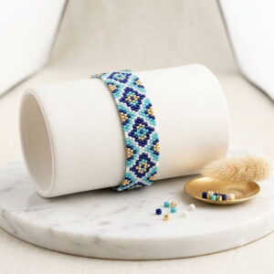 Blue mosaic pattern beaded bracelet displayed on a white cylindrical jewelry display with loose beads.