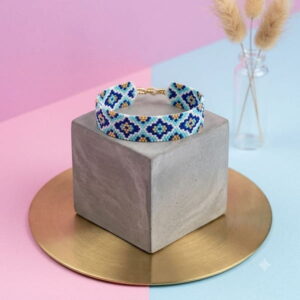 Blue mosaic pattern beaded bracelet displayed on a grey concrete cube and gold-toned tray.