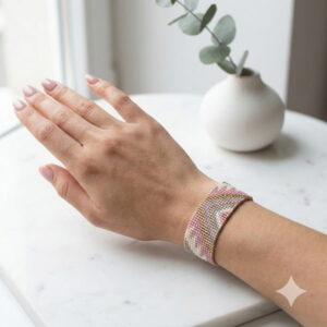 Top-down view of a delicate blush pink and metallic gold-finish woven seed bead bracelet on a wrist.