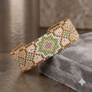 Close-up of the Boho Green and Cream Beaded Cuff Bracelet resting elegantly on a grey velvet jewelry box showing its gold-toned border.