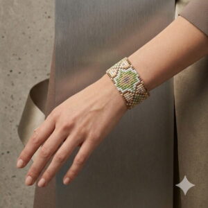 A close-up shot of a woman wearing the wide green, cream, and gold-toned beaded cuff bracelet on her wrist.