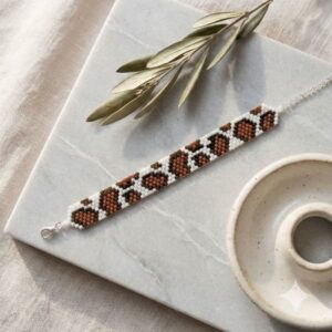 The flat-laid brown and white cow print beaded bracelet displaying its premium adjustable clasp and findings.
