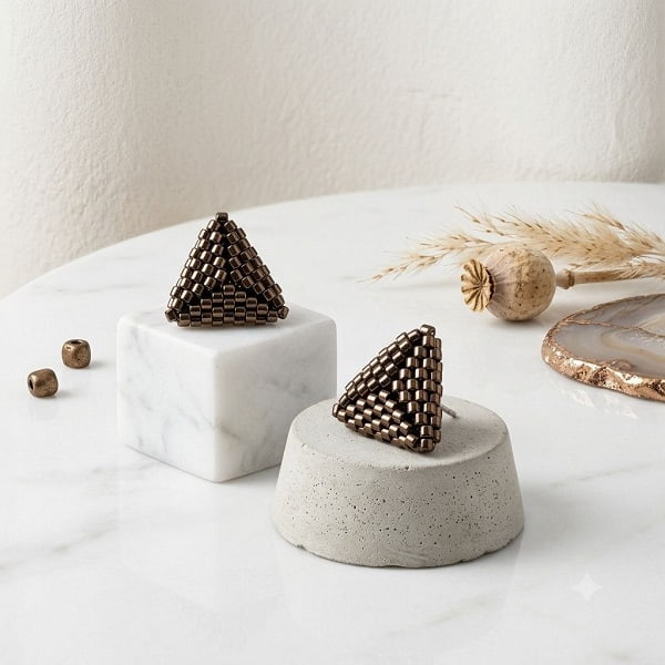 Handcrafted metallic gold-toned 3D beaded triangle earrings displayed on marble podiums.
