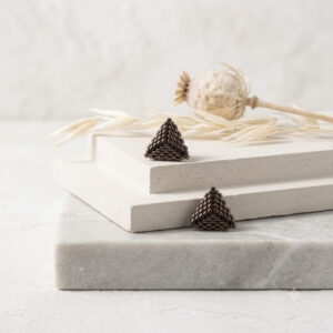 Studio display of gold-finish 3D geometric beaded triangle stud earrings on concrete slabs.