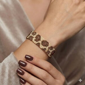 Close-up of a handmade brown and gold-toned geometric seed bead bracelet worn on a woman's wrist with brown nails.