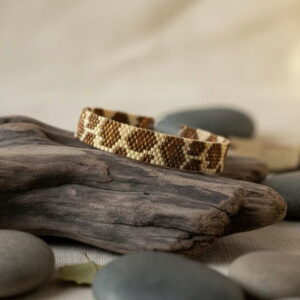 Handmade geometric beadwork bracelet with brilliant gold hues displayed beautifully on a piece of natural driftwood.