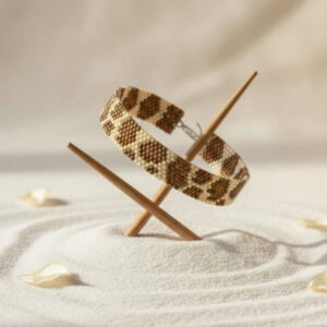 An artistic presentation of a geometric seed bead bracelet balancing on wooden sticks over textured white zen sand.