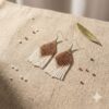 Pair of handmade caramel and cream beaded fringe earrings displayed on textured beige linen with loose artisan beads.