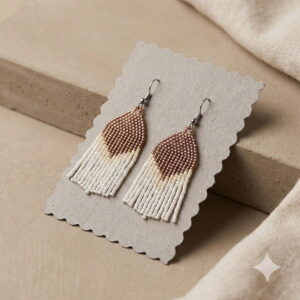 Artisan caramel brown and white beaded fringe statement earrings resting on a grey textured paper card presentation.