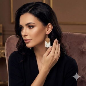 Profile view of a sophisticated model in a black top wearing the architectural gold-colored woven beaded earrings.