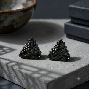 Pair of 3D black beaded pyramid earrings on concrete slab