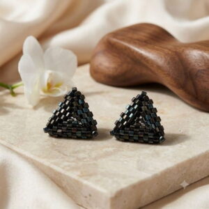 Handmade black triangle beaded earrings on marble display with white orchid