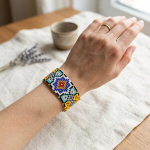 Top-down view of a hand wearing a colorful geometric woven glass bead bracelet.