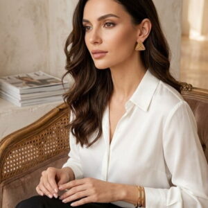 Model wearing gold-toned geometric beaded triangle earrings with a white silk blouse.