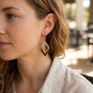 Side view profile of a woman wearing a gold and black handwoven beaded diamond earring outdoors.