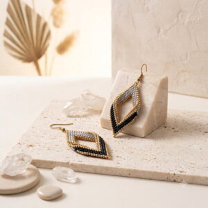 Gold and black beaded drop earrings displayed flat on travertine stone with raw crystals.