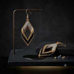 Gold-toned and black beaded geometric earring hanging on a brass display stand on dark slate.
