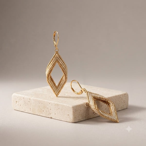 Pair of hand-beaded golden lattice diamond drop earrings on marble block.