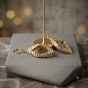 Gold-toned beaded twisted diamond earrings resting on grey jewelry display block.