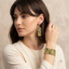 Woman wearing handcrafted golden green geometric beaded cuff bracelet and drop earrings.