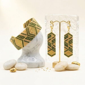 Handmade green and gold-toned beaded cuff bracelet wrapped on marble pedestal with earrings.